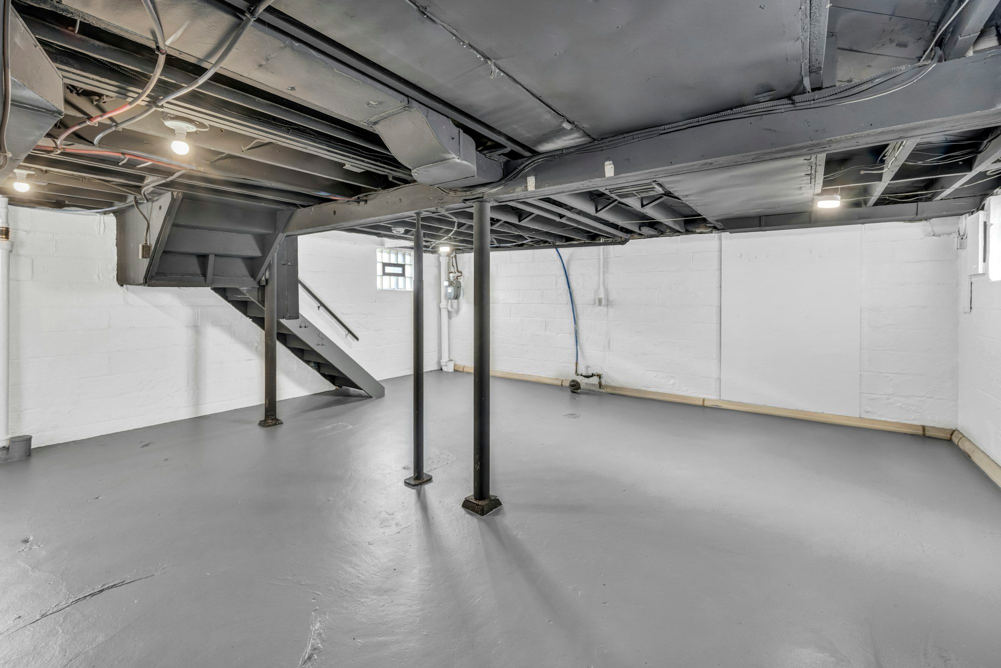 Unfinished basement with exposed joists, steel posts and an open stair