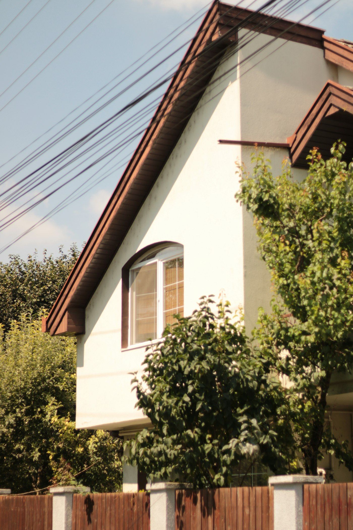 Two-story house with a gabled roof and an upstairs window behind trees