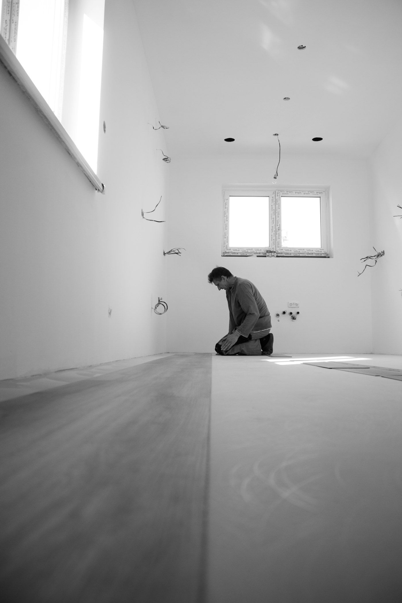 Installer kneeling at the far end of a bright room fitting planks