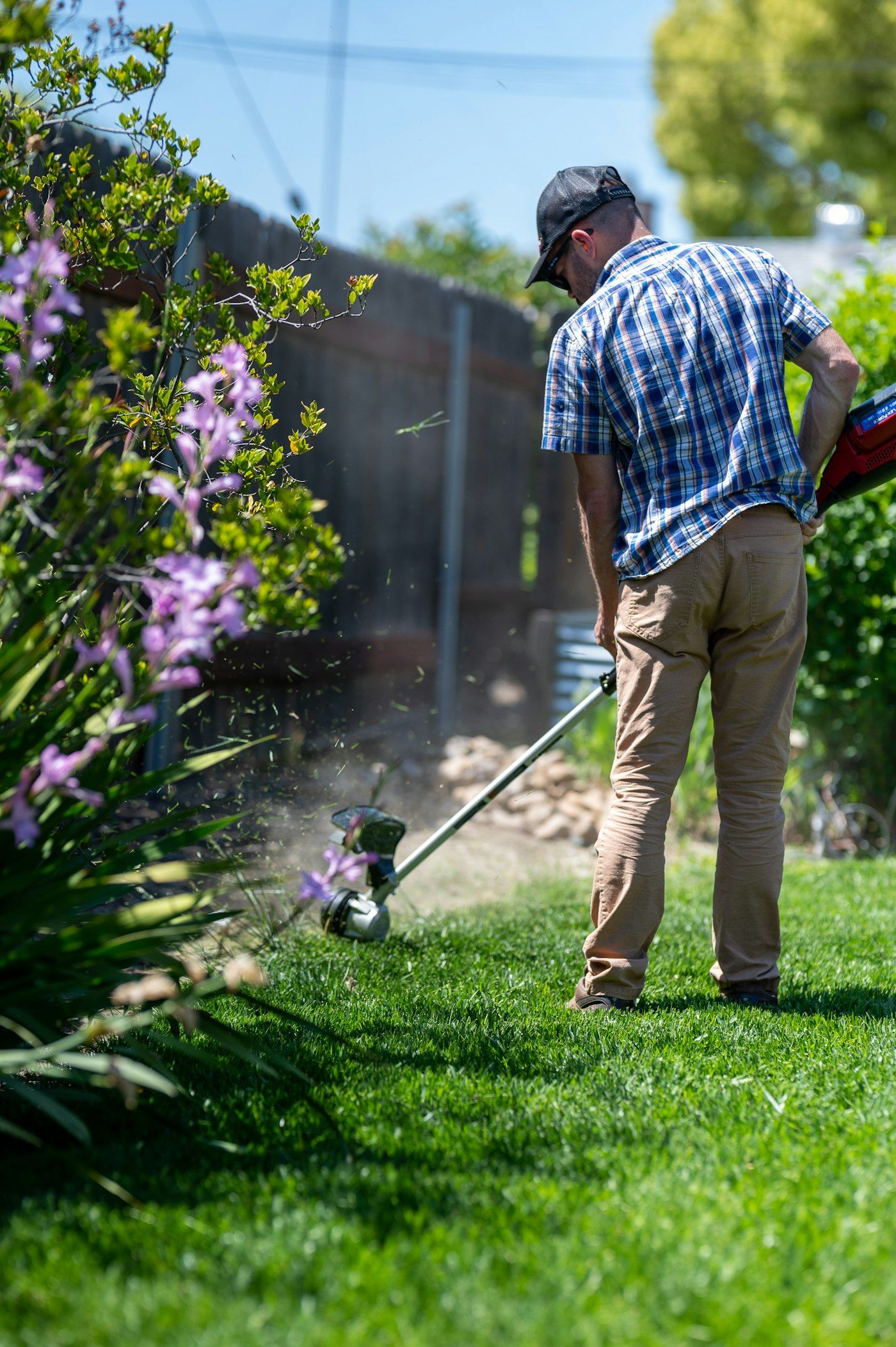 Crew member seen from behind trimming lawn edges beside a flower bed