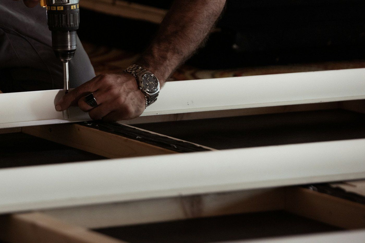 Installer's hand holding a rail steady while a drill drives a screw into the framing below