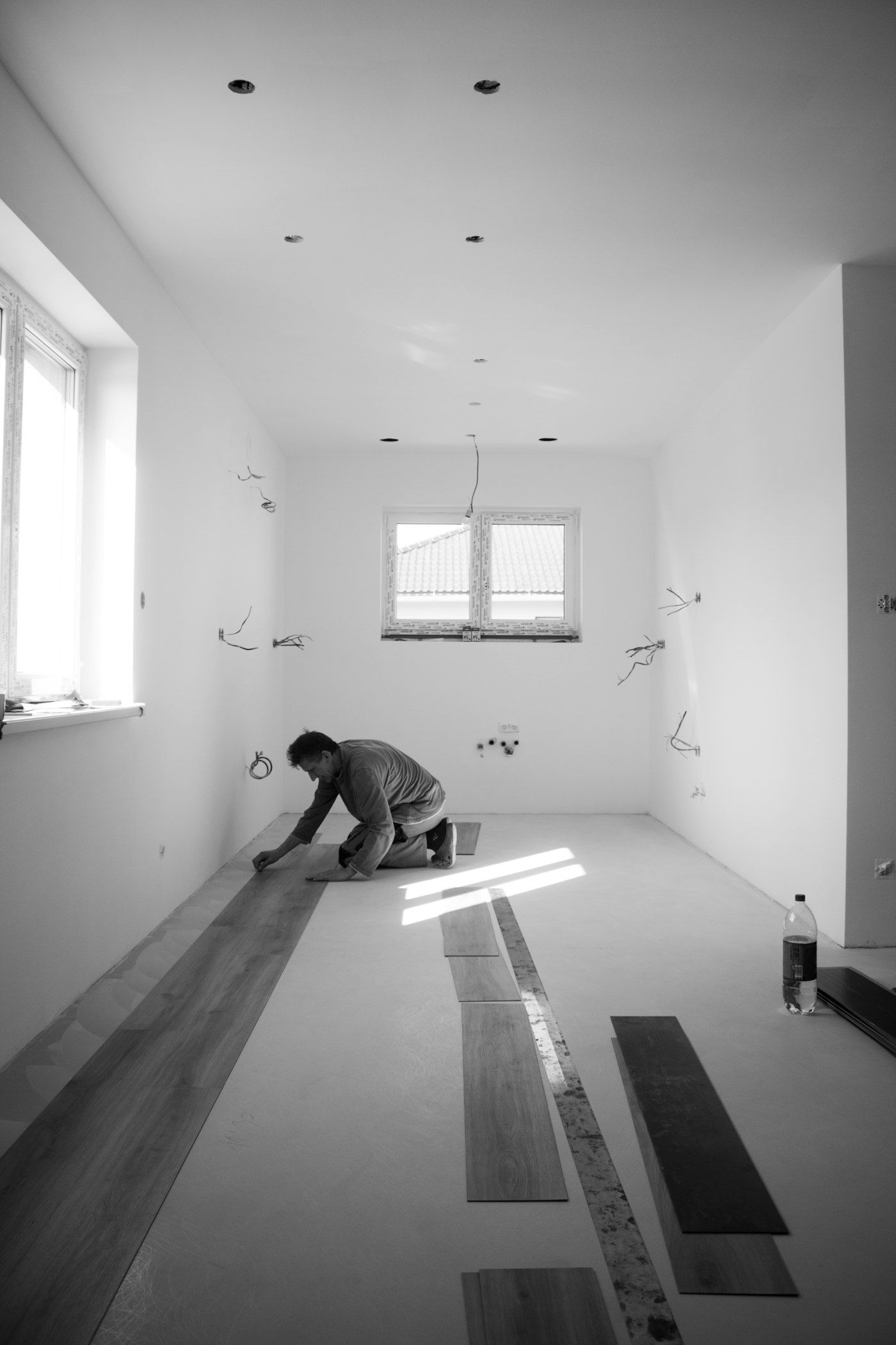 Installer kneeling in a bright empty room laying rows of planks