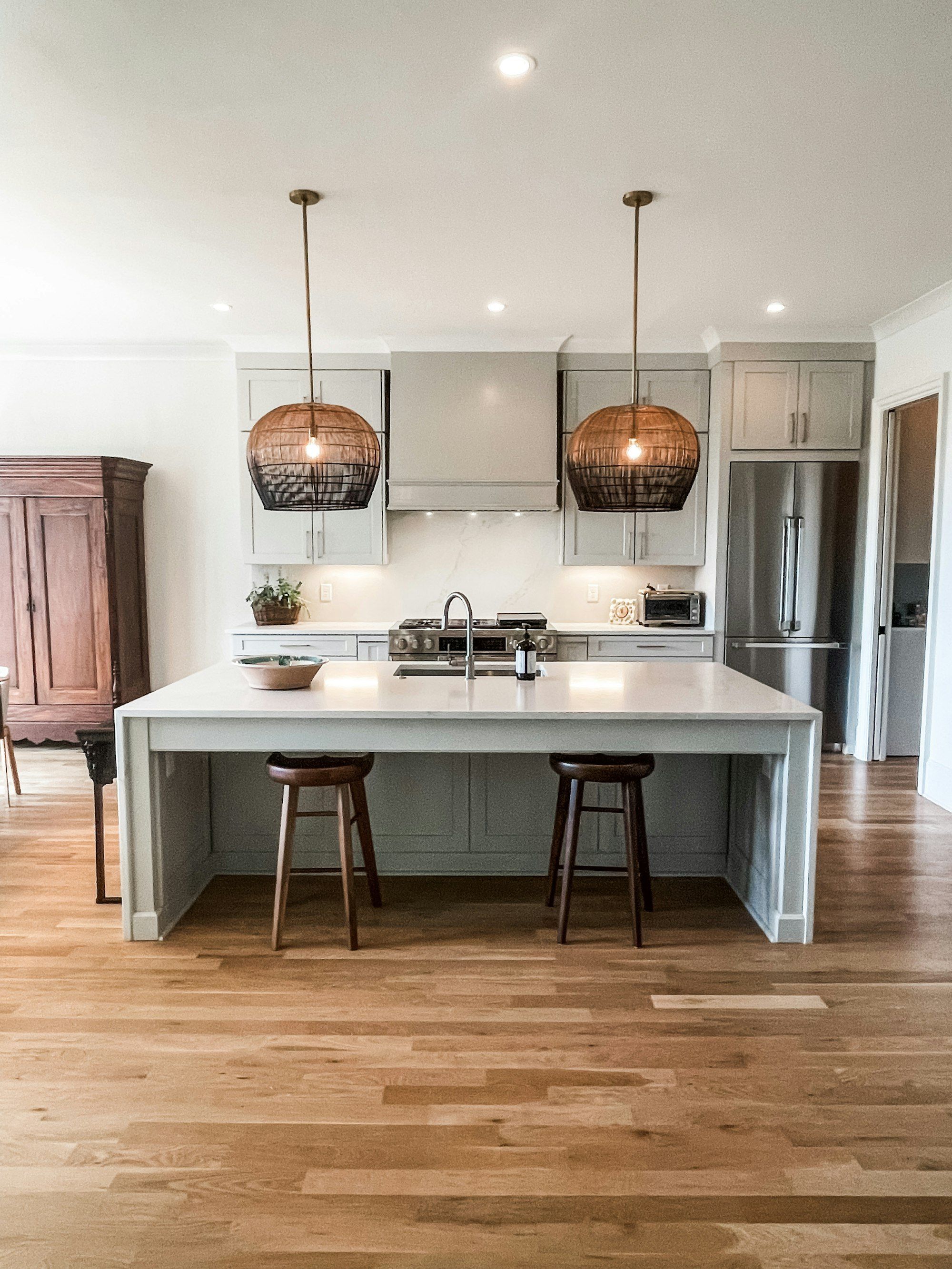 Kitchen with a pale green island, two wooden stools and a mixed-tone oak plank floor