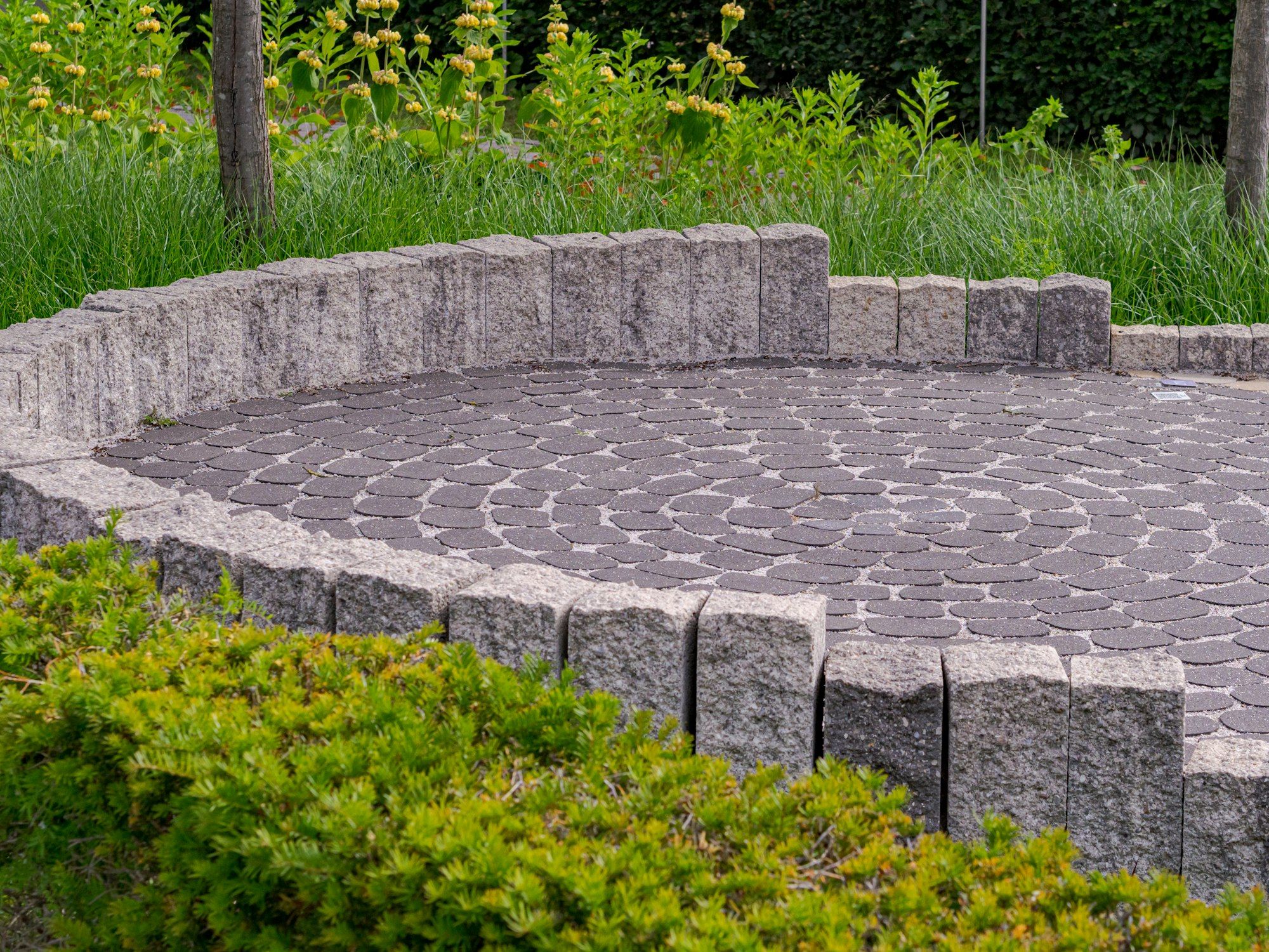 Circular cobblestone patio edged with a low granite seat wall