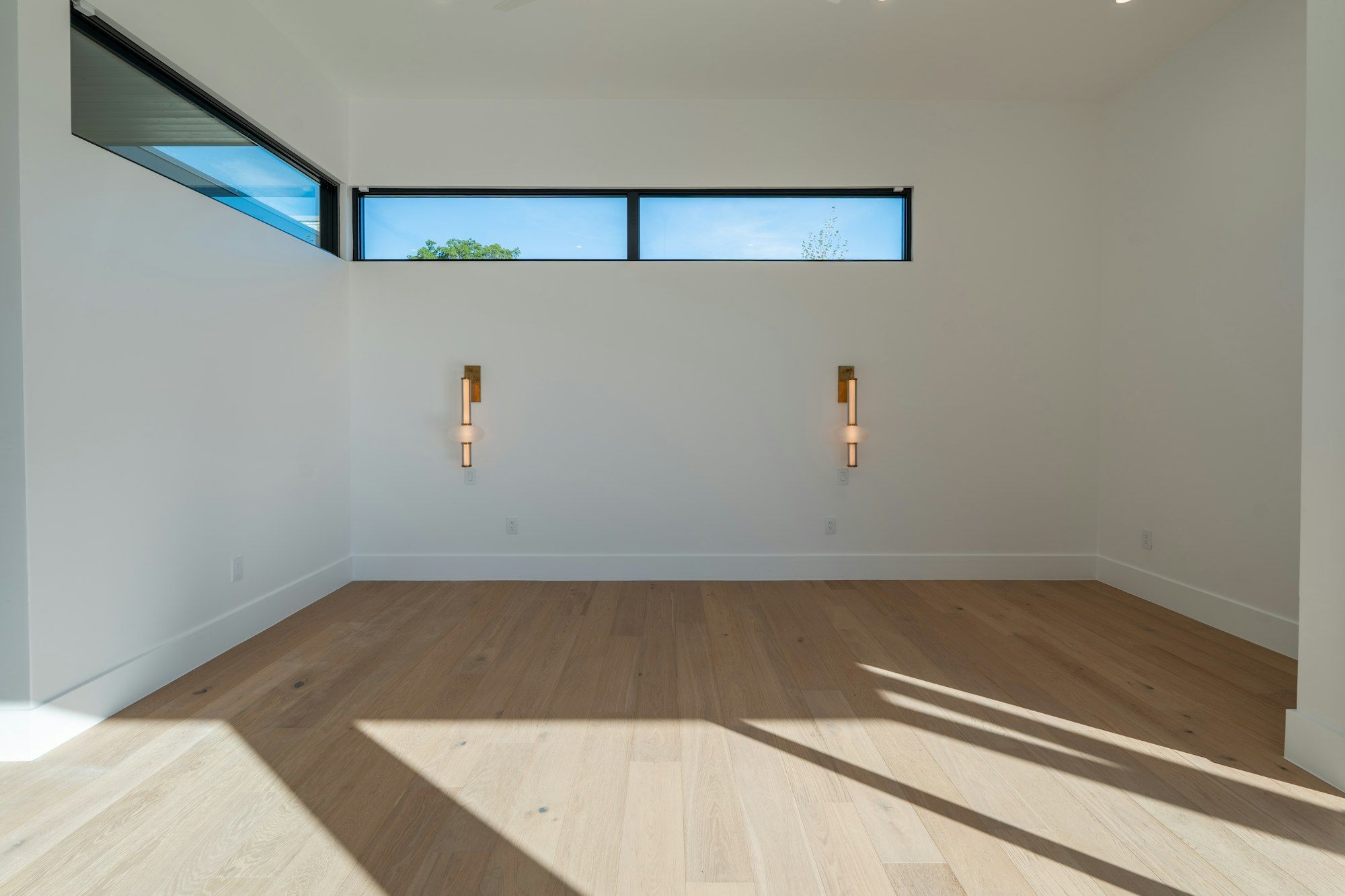 Empty white room with low sun across light white oak planks