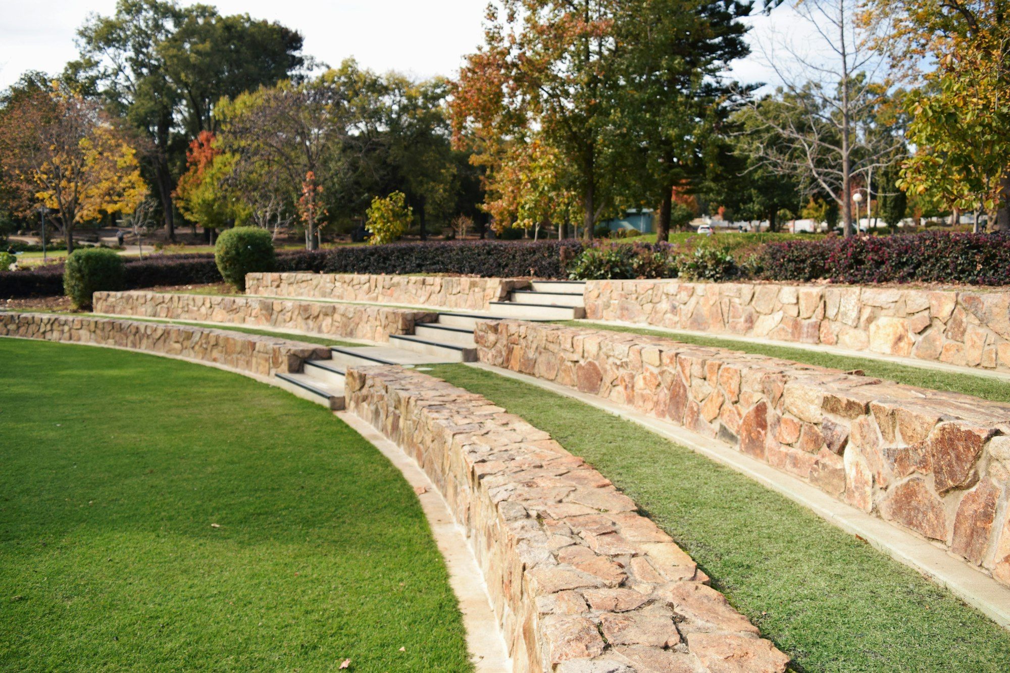 Curved terraces of natural stone retaining wall with lawn between each tier and stone steps leading up