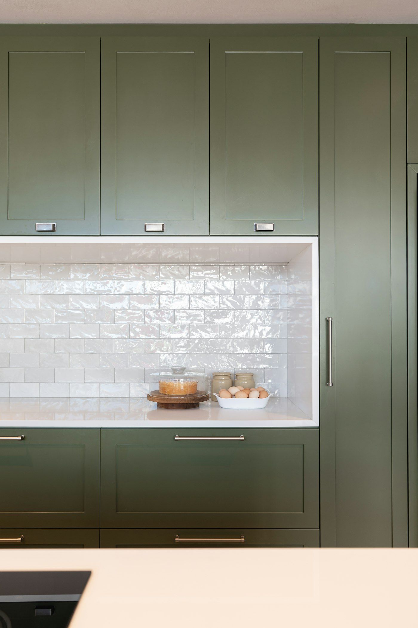 Green kitchen cabinets beside a white tiled niche