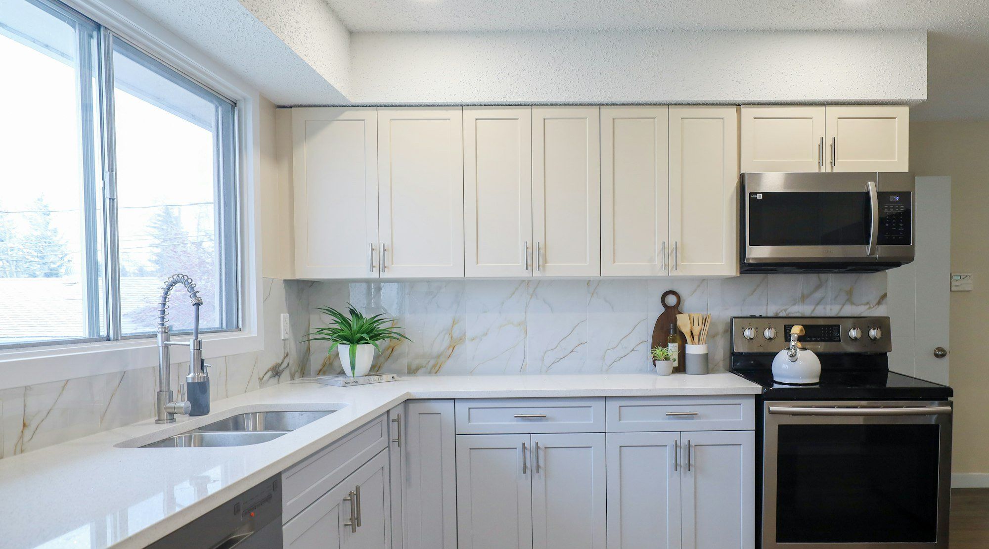 L-shaped white kitchen with quartz counters and a window over the sink