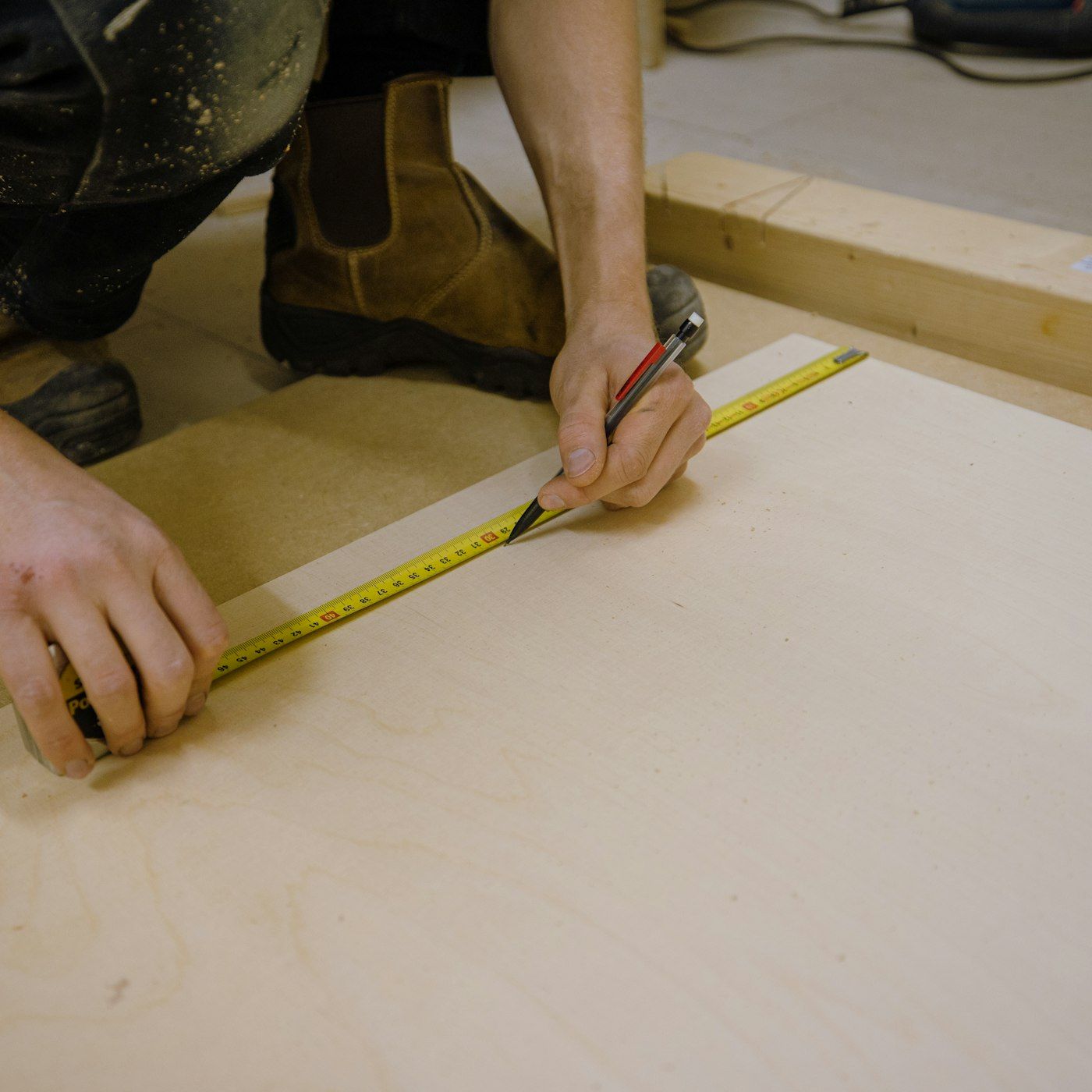 Carpenter marking a plywood sheet against a tape measure in the shop