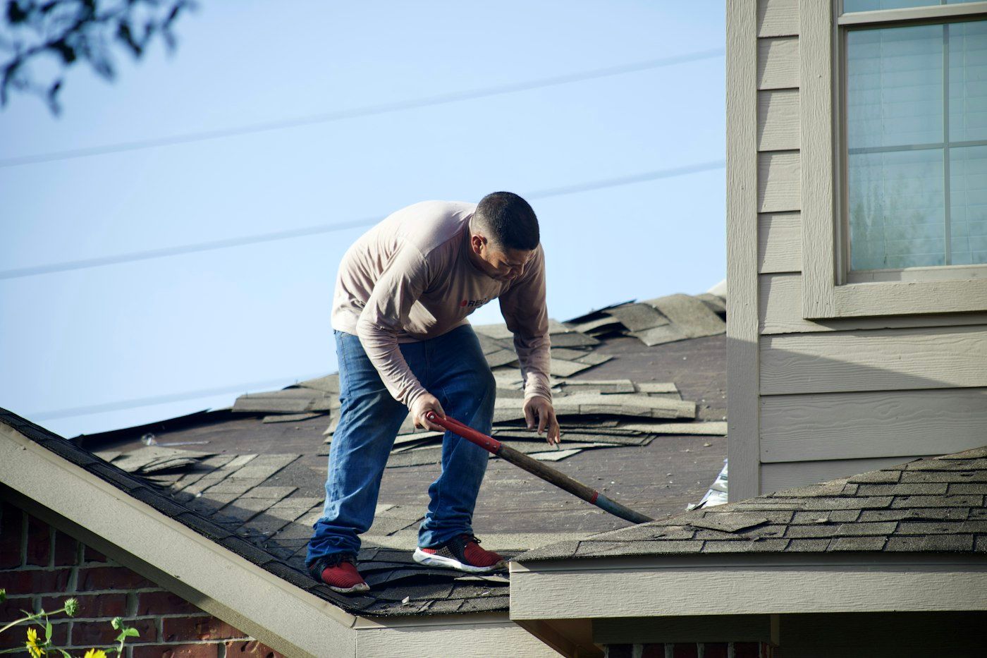 Roofer tearing off old asphalt shingles with a shovel on a brick house