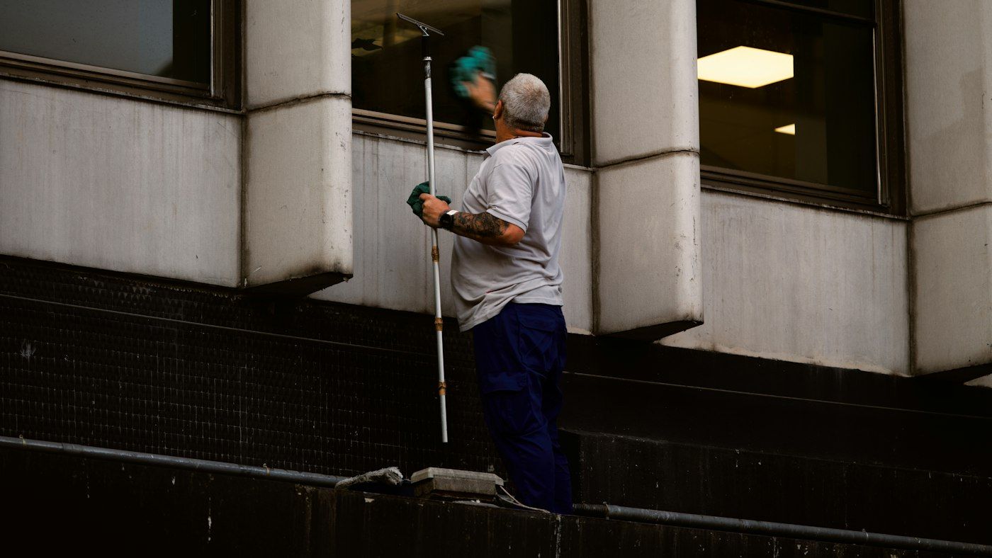 Window cleaner scrubbing an office window from outside with an extension pole