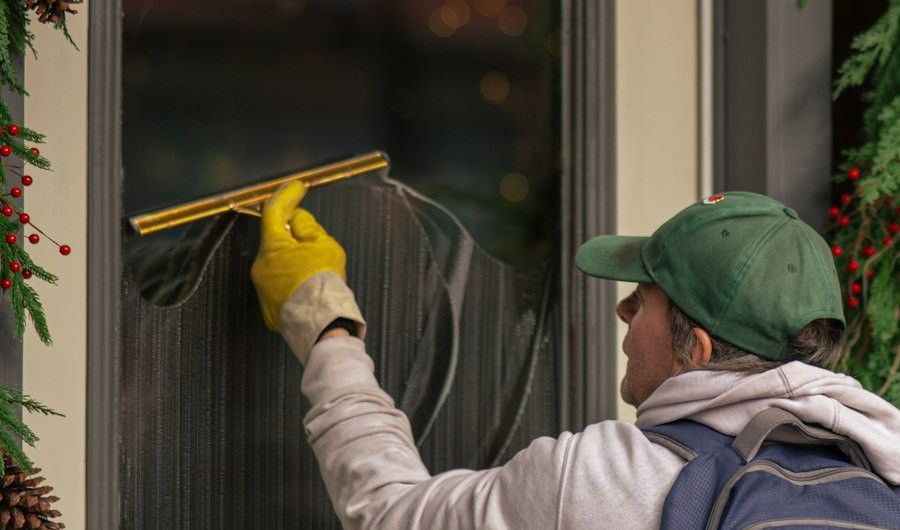 Window cleaner in yellow gloves running a squeegee down a shop door