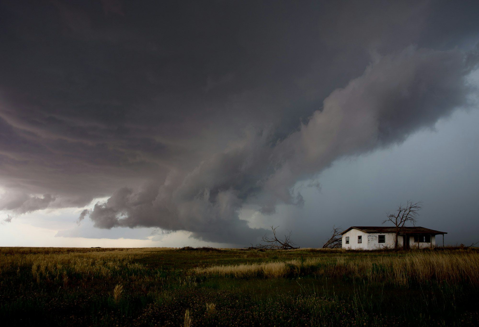 Dark supercell storm cloud rolling over a lone house on the plains