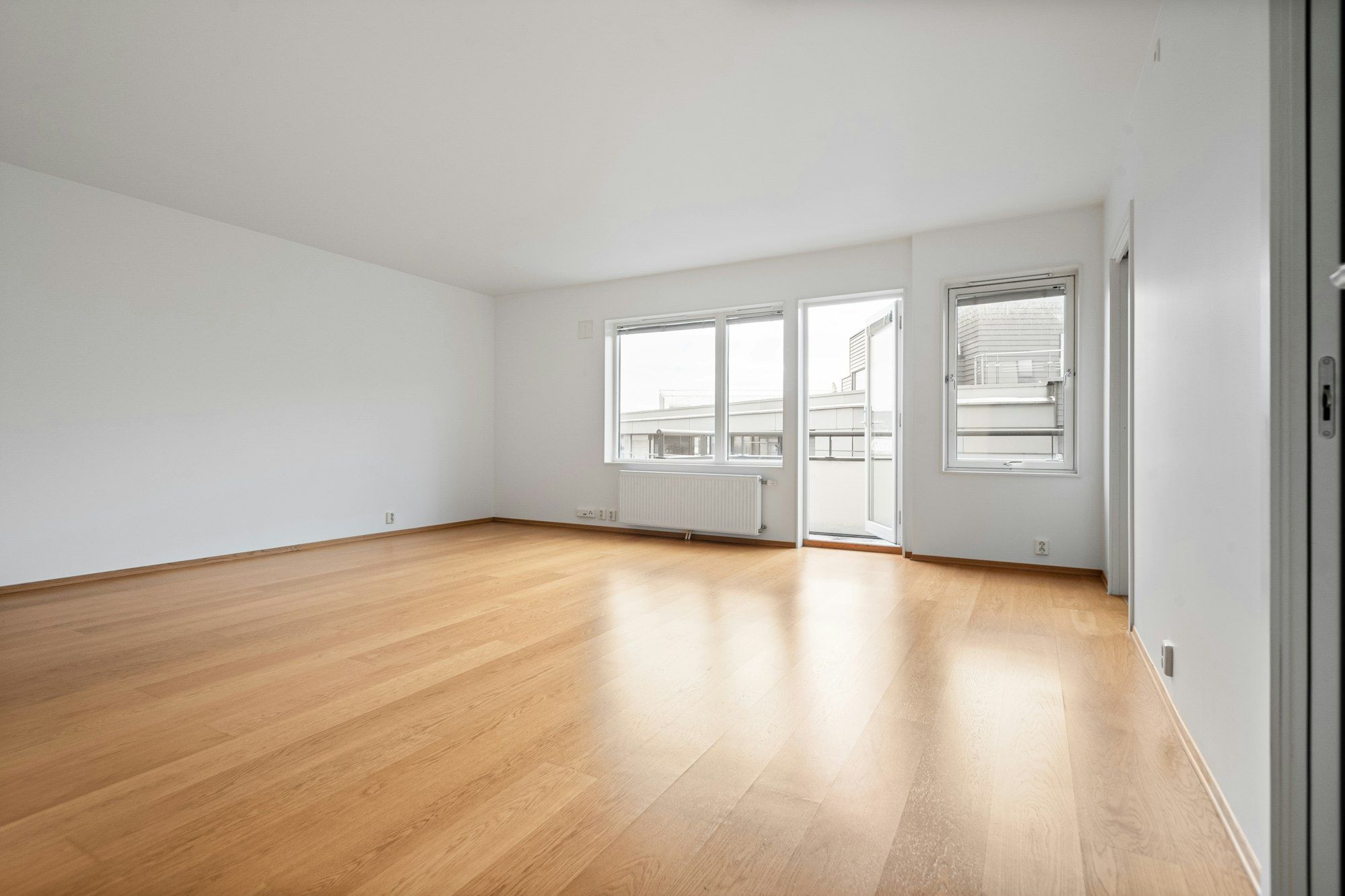 Empty living room with warm honey-toned red oak plank floor and a balcony door